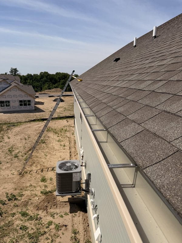 Close view along a shingled roof edge with a long gutter and its hangers on a newly built house