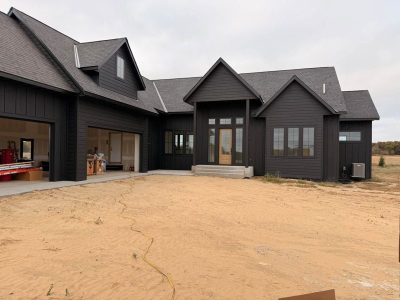 Wide black farmhouse-style house with dark gutters along the front roof edges and the garage