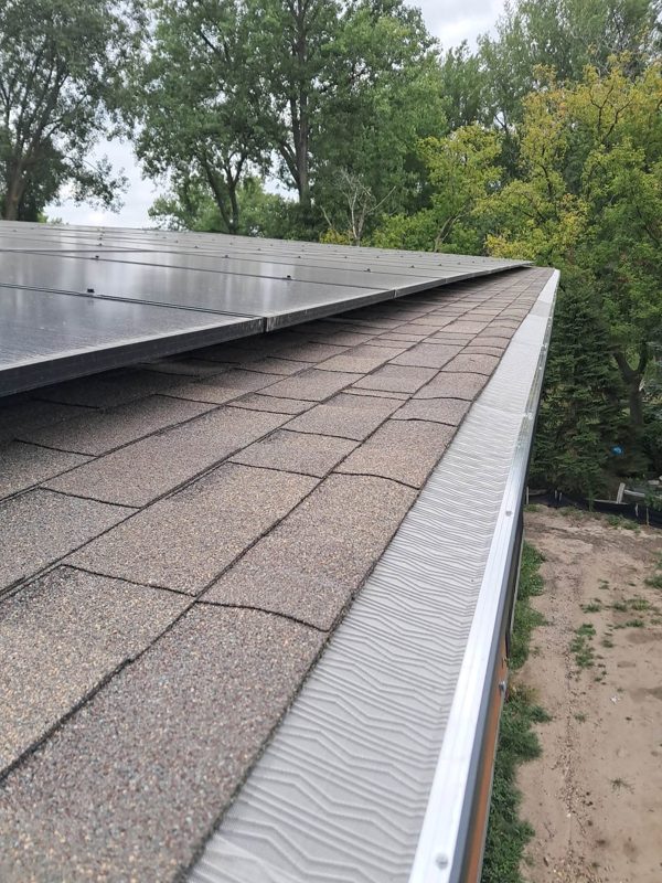 Close view of a gutter covered by a ridged gutter guard along a shingled roof edge