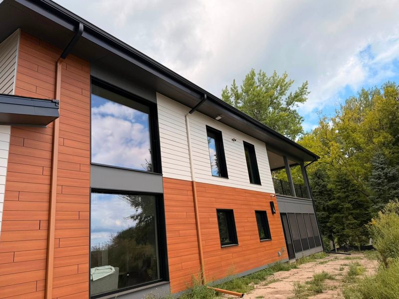 Modern house with orange and white siding and dark gutters and downspouts along the roofline